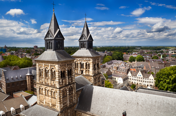 Blick auf die Doppeltürme der Basilika St. Servatius in Maastricht über den Dächern der Altstadt unter wolkigem Himmel.