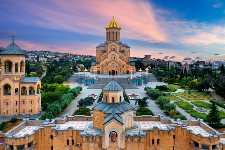 Sameba-Kathedrale in Tiflis mit goldener Kuppel, großer Freitreppe, symmetrischer Gartenanlage und Abendhimmel in zarten Farben.