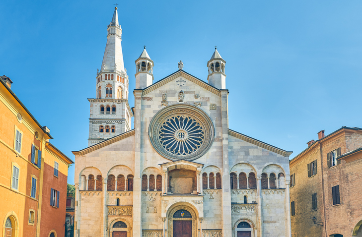 Fassade des Doms von Modena mit großer Rosette, romanischen Bögen und der Torre della Ghirlandina vor blauem Himmel.