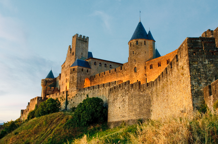 Die beleuchteten Mauern und Türme der Festung Carcassonne stehen auf einem Hügel vor dem Abendhimmel.