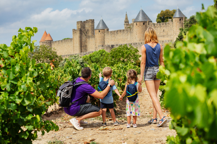 Eine Familie mit zwei Kindern läuft durch Weinreben auf die Stadtmauer von Carcassonne zu.