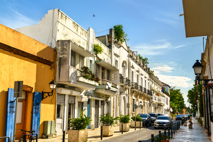 Historische Straße mit hellen Fassaden, Balkonen und parkenden Autos in Santo Domingo