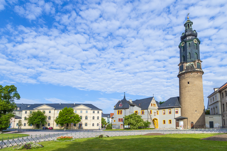 Ein großer Platz mit Rasenfläche, hellem Gebäudeensemble und hohem Turm unter wolkigem Himmel in Weimar.