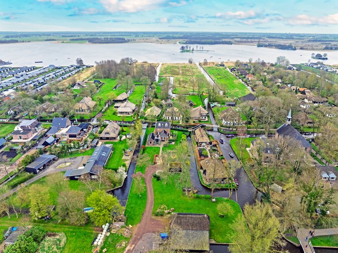 Luftbild von Giethoorn mit Bauernhäusern, Kanälen, Wiesen und großem See im Hintergrund.