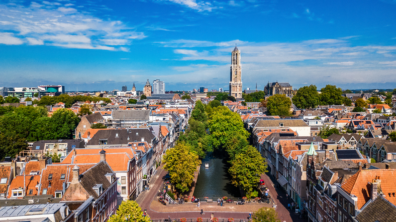 Panoramablick über Utrecht mit Oudegracht, roten Ziegeldächern, grünen Bäumen und dem hohen Domturm am Horizont.