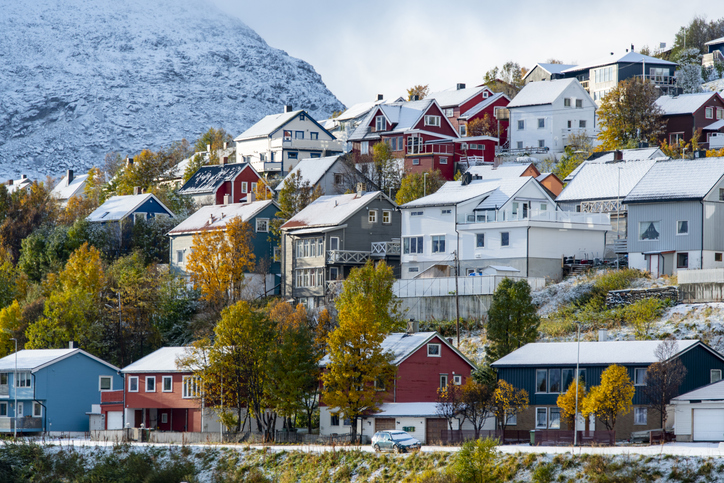 Farbenfrohe Wohnhäuser in Hammerfest mit verschneiten Dächern, herbstlichen Bäumen und schneebedecktem Berghang im Hintergrund.