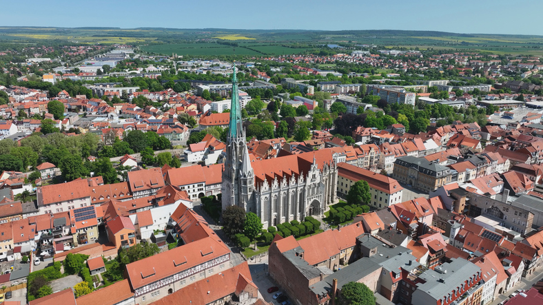 Luftaufnahme der Erfurter Altstadt mit großer gotischer Kirche, dicht bebauten Straßenzügen und grünen Stadtbereichen.