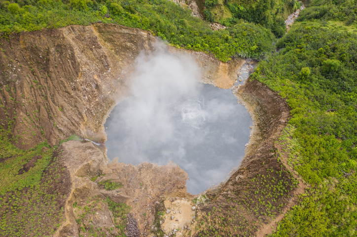 Luftaufnahme eines dampfenden Kratersees auf Dominica, umgeben von steilen Hängen, grüner Vegetation und vulkanischer Landschaft.
