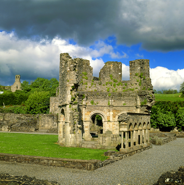 Historische Steinruinen von Mellifont Abbey bei Drogheda mit Mauerresten, Torbögen und grünem Gelände unter dramatischem Himmel.
