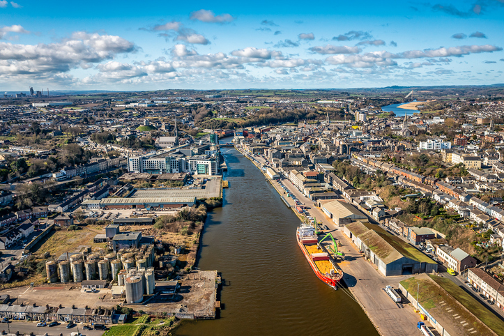 Luftaufnahme von Drogheda mit dem Fluss Boyne, Hafenanlagen, Frachtschiff und weitläufigem Stadtgebiet unter wolkigem Himmel.