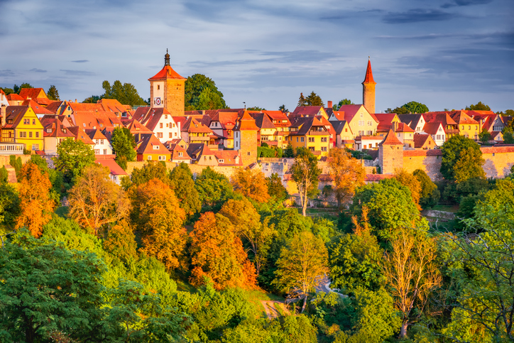 Blick auf Rothenburg ob der Tauber mit Stadtmauer, Türmen und herbstlich gefärbten Bäumen im warmen Abendlicht.