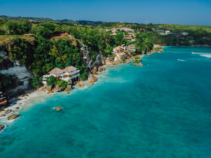 Luftaufnahme einer Küste mit türkisblauem Wasser, Felsen und Gebäuden direkt am Meer