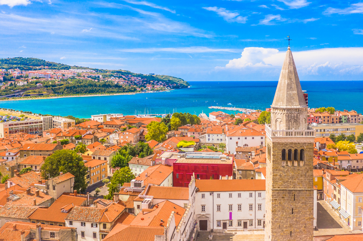 Blick über die Dächer von Koper mit Kirchturm, Meer und Küstenlandschaft im Hintergrund