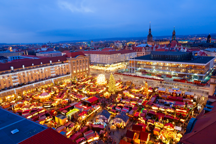 Blick von oben auf den beleuchteten Dresdner Striezelmarkt am Altmarkt mit zahlreichen Weihnachtsständen, Weihnachtsbaum und Riesenrad in der Abenddämmerung.