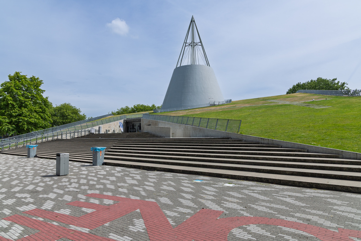 Ein modernes kegelförmiges Gebäude steht auf einer begrünten Anhöhe mit breiten Treppen in Delft.