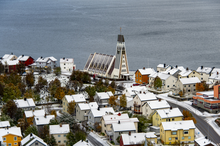 Kirche von Hammerfest mit markantem modernem Turm zwischen verschneiten Wohnhäusern und Straßen nahe der Küste.
