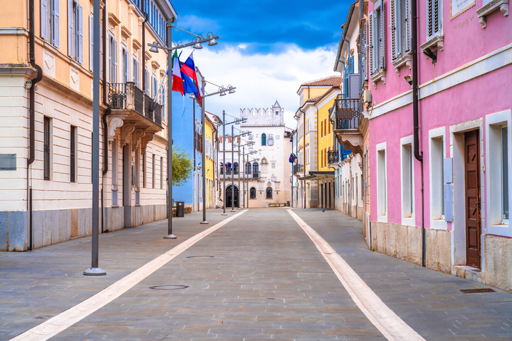 Ruhige Straße mit pastellfarbenen Häusern und Blick auf ein historisches Gebäude in Koper