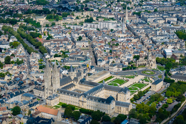 Luftaufnahme von Caen mit großem historischen Klosterkomplex, grünen Anlagen, dicht bebauter Innenstadt und breiten Straßenachsen.