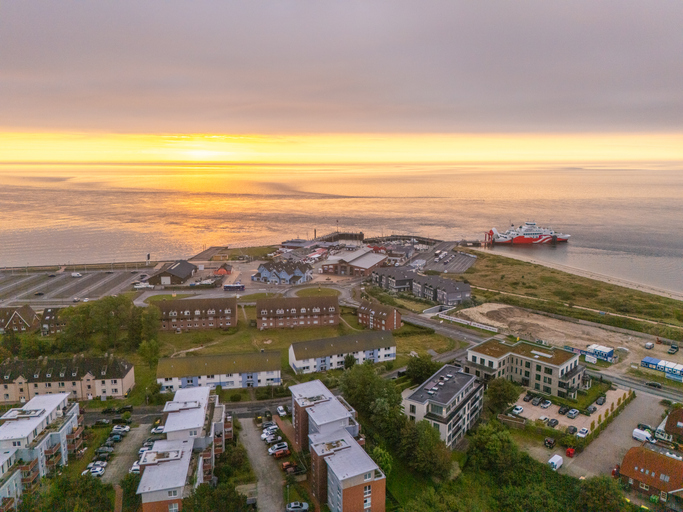 Hafen auf Sylt mit Fähre, Wohngebäuden und ruhigem Meer bei stimmungsvollem Sonnenuntergang.