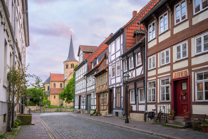 Ruhige Altstadtgasse in Hildesheim mit Fachwerkhäusern, Kopfsteinpflaster, Fahrrad und historischem Kirchturm im Hintergrund.