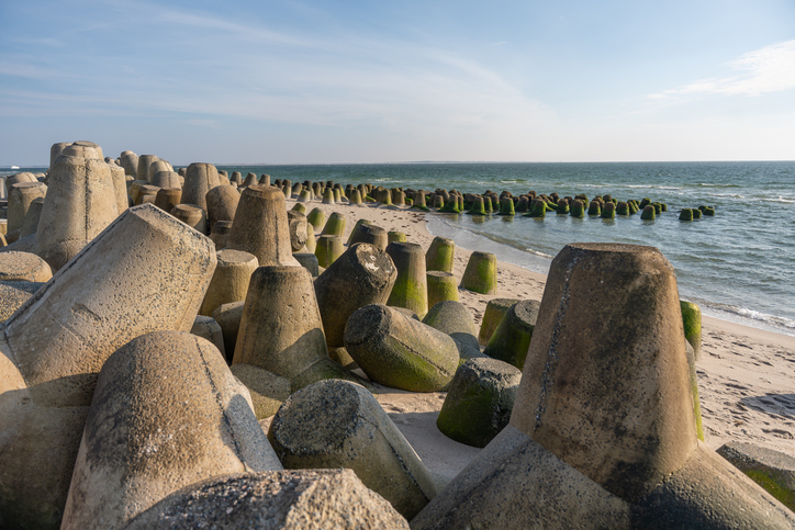 Große Betonblöcke als Küstenschutz an einem Strand auf Sylt mit Nordseewellen, Sand und moosbewachsenen Wellenbrechern.