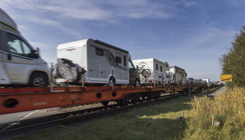Autozug mit Wohnmobilen auf dem Weg nach Sylt an einer Bahnstrecke mit sichtbarem Ortsschild Klappholttal.