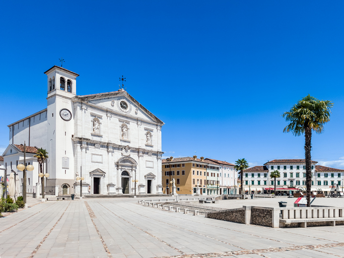 Weiße Fassade der Kathedrale von Palmanova mit Glockenturm und Palme auf der Piazza Grande