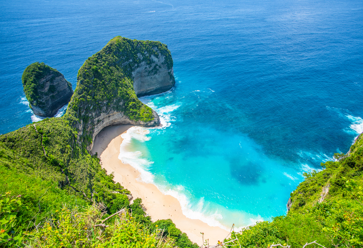 Hohe grüne Klippen und ein heller Sandstrand mit türkisblauem Wasser an einer spektakulären Küste