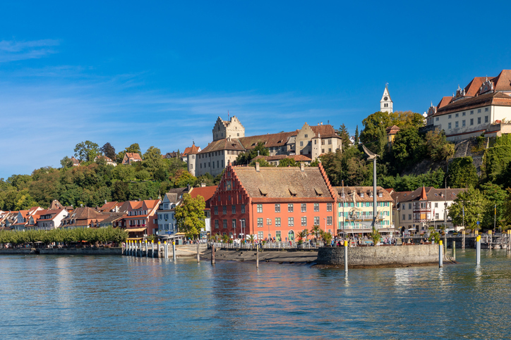 Bunte Häuser am Ufer von Meersburg liegen vor einem Hang mit historischen Gebäuden und einer Kirche.