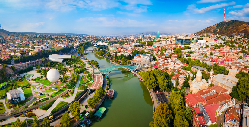 Panorama von Tiflis mit Friedensbrücke, Kura-Fluss, modernen Gebäuden, Kirchen und dicht bebauten Stadtvierteln.