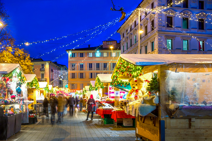 Beleuchteter Weihnachtsmarkt in Basel mit geschmückten Holzhütten, Lichterketten, Besuchern und festlicher Dekoration am Abend.