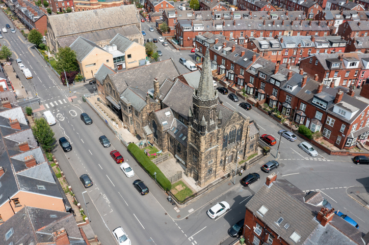 Luftaufnahme einer historischen Steinkirche in Leeds zwischen roten Backsteinhäusern, Straßen und dichter Wohnbebauung.