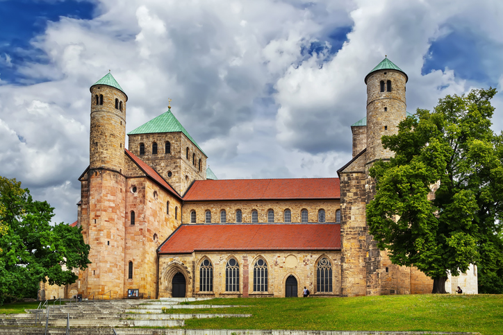 Kirche St. Michaelis in Hildesheim mit romanischer Natursteinfassade, roten Dächern, Rundtürmen und grünen Turmhelmen.