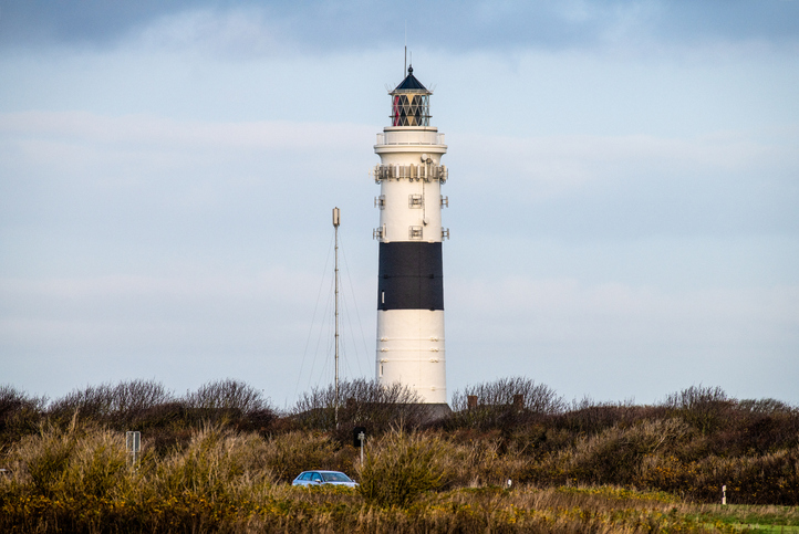 Schwarz-weißer Leuchtturm auf Sylt über flacher Dünenlandschaft und Sträuchern unter hellem Himmel.