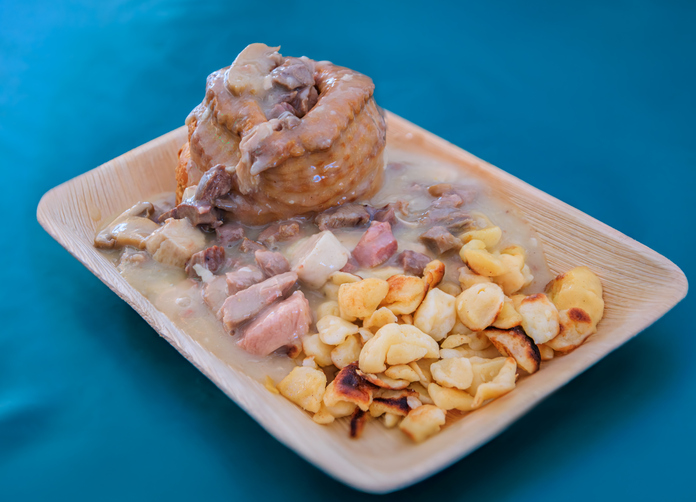 Ein herzhaftes elsässisches Gericht mit Fleisch, cremiger Sauce und gebratenen Nudeln liegt auf einem Holzschälchen.
