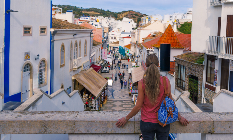 Blick über eine Treppe auf eine belebte Gasse in der Altstadt von Albufeira mit weißen Häusern, kleinen Geschäften und Menschen.