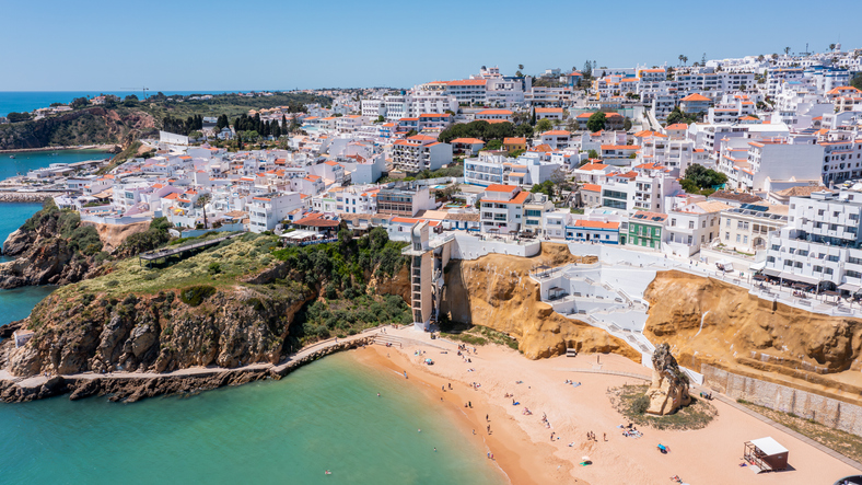 Luftaufnahme von Albufeira an der Algarve mit heller Altstadt, steilen Klippen, Sandstrand und türkisblauem Meer.