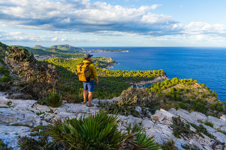Wanderer blickt von einem felsigen Aussichtspunkt auf die Küste und das Meer bei Canyamel