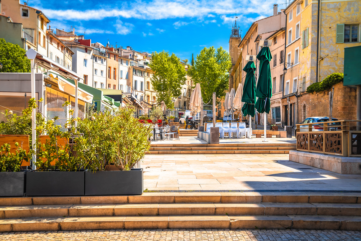 Ein offener Platz mit Stufen, Sonnenschirmen und Cafés liegt zwischen hellen Häusern in Aix-en-Provence.