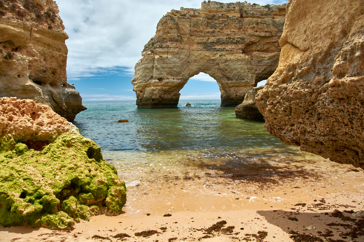 Kleine Bucht bei Albufeira mit sandigem Ufer, ruhigem Wasser und einem natürlichen Felsbogen in den goldenen Klippen.
