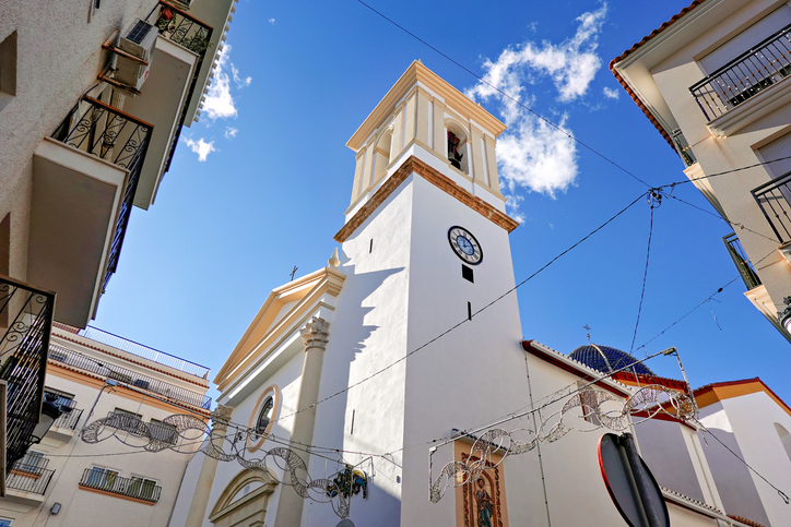 Weiße Kirche mit Glockenturm in einer engen Straße der Altstadt von Benidorm
