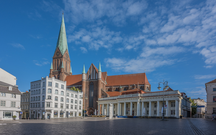 Ein großer gotischer Kirchenbau erhebt sich hinter einem offenen Platz mit hellen Gebäuden im Zentrum von Schwerin.