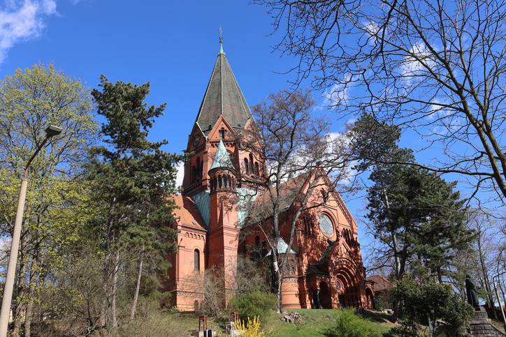 Historische Backsteinkirche in Görlitz mit hohem Turm, spitzem Dach und grüner Umgebung unter blauem Himmel.