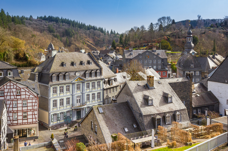 Erhöhter Blick auf Monschau mit historischen Schieferhäusern, Fachwerk, Kirche und dicht bebauter Altstadt zwischen bewaldeten Hängen.