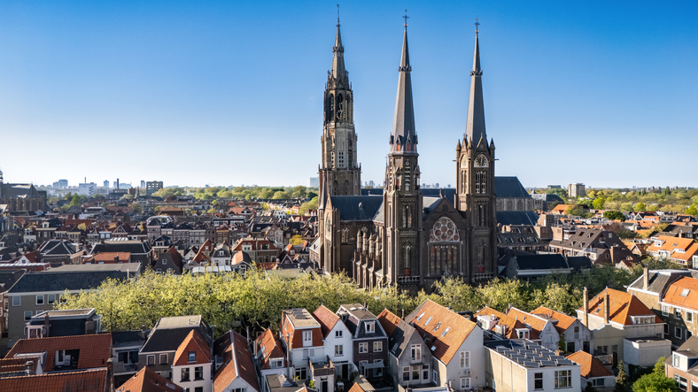 Mehrere hohe Kirchtürme und eine große Kirche ragen über die Dächer der Altstadt von Delft hinaus.