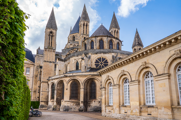 Historische Kirche in Caen mit romanischer Architektur, mehreren Türmen, Rundbogenfenstern und angrenzenden Natursteingebäuden.