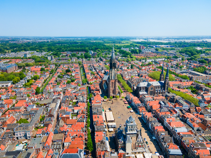 Ein Luftbild zeigt die Altstadt von Delft mit roten Dächern, breiten Plätzen und markanten Kirchtürmen.