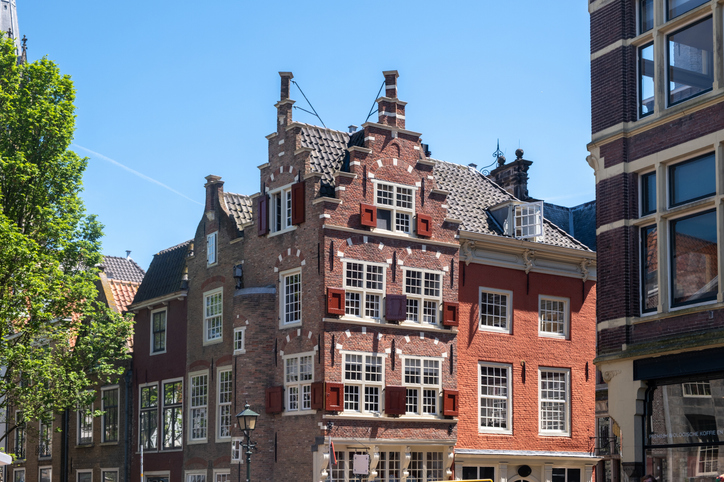 Ein rotes Backsteingebäude mit verziertem Giebel steht zwischen weiteren historischen Häusern in Delft.