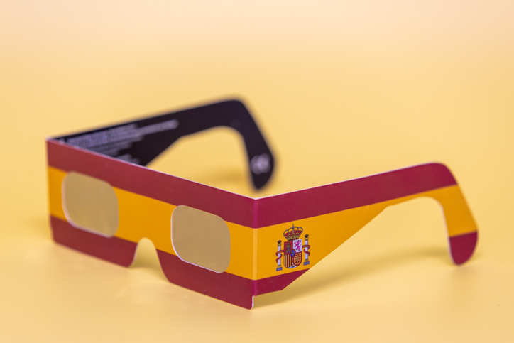 Sonnenfinsternisbrille in den Farben der spanischen Flagge mit spanischem Wappen vor gelbem Hintergrund.