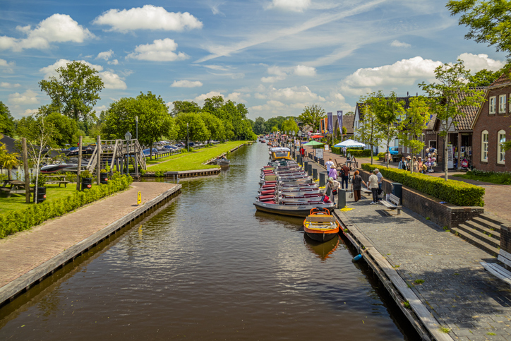 Kanal in Giethoorn mit kleinen Ausflugsbooten am Ufer, Spazierweg und Besuchern bei sonnigem Wetter.